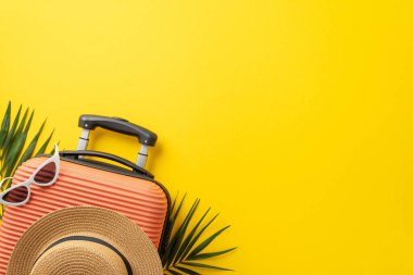 Ada gezisi konsepti. Üzerinde hasır şapka ve güneş gözlüğü olan turuncu bavul resmi. Palmiye yaprakları ve kopyalanmış sarı arka plan.