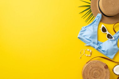 Yaz tatili kavramı. Güneş şapkası, mavi bikinili fotoğraf, güneş gözlüğü ve kabuk bilezikli saman çantalı kopyalanmış sarı arka plan.