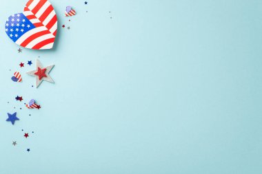 İşçi Bayramı kutlaması. Vatansever süslemelerin genel görünümü: kalp şeklinde Amerikan bayrağı tasarımları, ışıldayan yıldızlar, konfetiler, metin veya reklam için boş bir alanı olan pastel mavi arkaplan üzerine kuruludur.