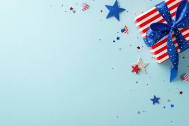4 Temmuz şerefe. Sembolik süslemelerin üst perspektifi: Amerikan bayrağından esinlenilmiş ışıldayan yıldızlar, konfeti, temalı hediye kutusu, metin veya tanıtım içeriği için boş alanı olan pastel mavi taban
