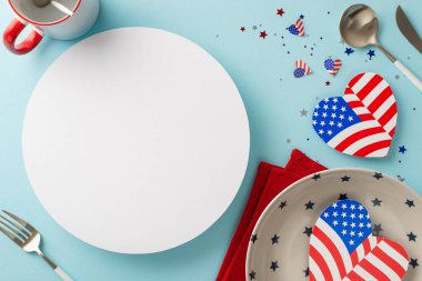 Amerika 'nın Bağımsızlık Günü' ne sanatsal masa gösterisiyle hazır olun. Tabak, çatal bıçak, kupa, peçete, Amerikan bayrağıyla kalpler, pastel mavi arka planda konfeti, metin veya reklam için kullanılabilir daire.