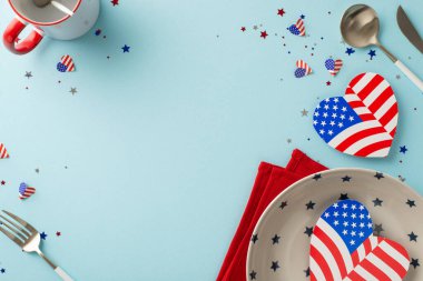 Amerika 'nın Bağımsızlık Günü' ne şık masa düzenlemeleriyle hazır olun. Üst manzara tabağı, çatal bıçak, bardak, peçete, bayrak tasarımı, konfeti, pastel mavi arka plan, metin veya tanıtım alanı