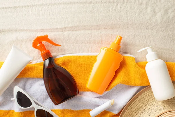 stock image Sunburn prevention concept. Above view photo of orange towel with tube,spray and bottle of sunscreen, sunglasses and straw hat on the sand on isolated background with copyspace