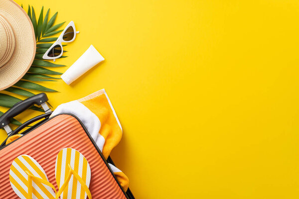 Sun-soaked dreams. Top view setup displaying a suitcase, beach essentials, glasses, sunhat, sunscreen, flip-flops, towel, palm leaf on vibrant yellow backdrop. Empty space provided for text or adverts