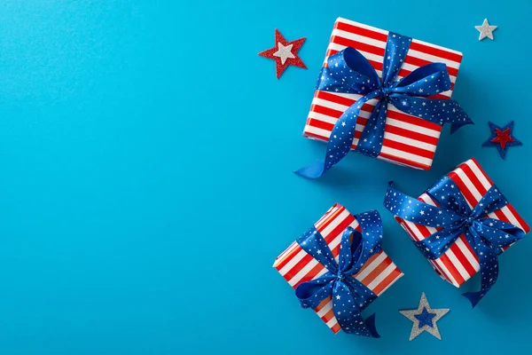 Embrace patriotic atmosphere of USA\'s Independence Day with captivating top view showcasing glistening stars and gift boxes adorned in USA flag motifs, against blue backdrop that invites text or ad