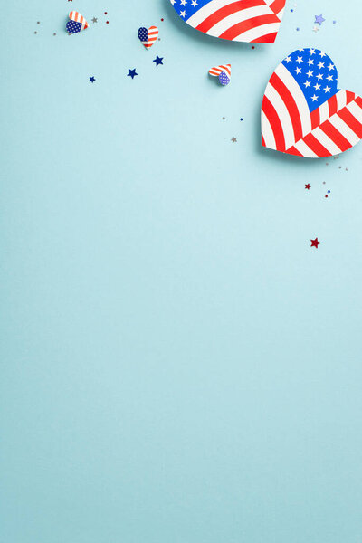 Wishing joyful Independence Day to America! Vertical overhead shot of patriotic-themed embellishments, such as hearts with American flag pattern, confetti on soft blue backdrop with space for promo