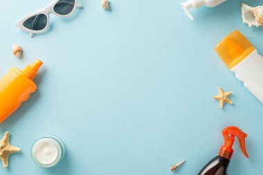 Sağlıklı yaz bronzlaşması. Güneş kremi şişeleri, spreyler, kremler, deniz kabukları ve güneş gözlükleriyle çevrili, açık mavi izole arkaplan ve fotokopi alanı