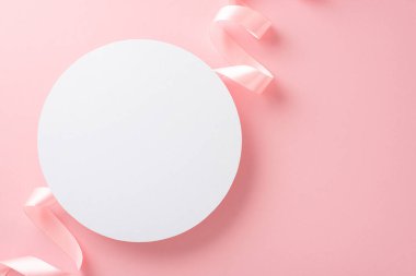 İzole edilmiş açık pembe arkaplanlı, pastel pembe kurdeleli boş beyaz dairenin üst görünüm fotoğrafı.
