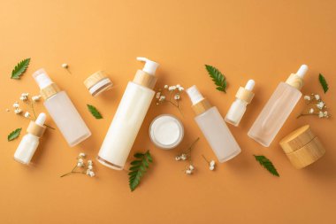 Organik kozmetik ürünler konsepti. Kozmetik kavanozlarının, şişelerin ve tüplerin, eğreltiotu yapraklarının ve bej renkli izole arkaplandaki beyaz çıngıraklı çiçeklerin en üstteki fotoğrafı.
