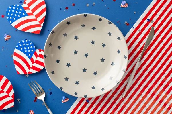 Amerikan Bağımsızlık Günü kutlamaları için menüyü seçin. Boş tabak, çatal bıçak takımı, Amerikan bayrağı, parlak konfeti sergilenen kalpler, metin veya reklamlar için alanı olan ulusal bayrak arka planı olan masa manzarası