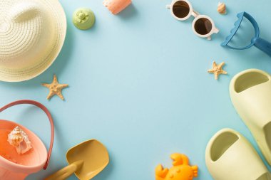 Çocuk konseptiyle tatil. Çocuk plaj oyuncakları, panama, parmak arası terlik, güneş gözlüğü ve mavi izole arkaplanda deniz kabukları ile çevrili boş bir alanın dikey fotoğrafı.