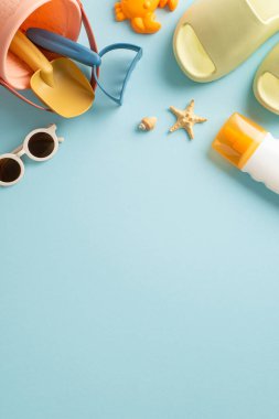 Tatil konseptinde çocuklar için eğlenceli aktiviteler. Terliklerin ve güneş gözlüklerinin dikey resmi, plaj çocuk oyuncakları, güneş kremi ve kabuklar mavi izole edilmiş arka planda fotokopi alanı ile