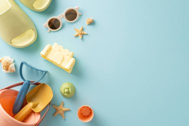 Çocuk plajı aktiviteleri konsepti. Sahildeki oyuncakların, terliklerin, güneş gözlüklerinin ve deniz kabuklarının yüksek açılı görüntüsü ve fotokopi alanı ile izole edilmiş mavi arka plan.