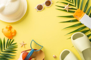 Çocuklu tropik bir tatil köyü. Palmiye yaprakları ve deniz kabukları, kum oyuncakları, güneş kremi şişesi, sarı izole arka planda panama olan terlikler ile çevrili boş bir yerin en üstteki fotoğrafı.