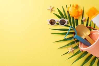 Tatil konseptinde çocuklar için eğlenceli aktiviteler. Güneş gözlüğü, plaj oyuncakları, güneş kremi, palmiye yaprağı ve kabuklu sarı izole arkaplan ve fotokopi alanı ile boş alanın en üstteki resmi.