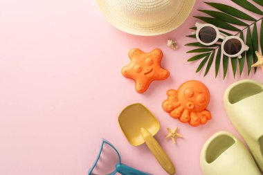 Çocuk konseptiyle yaz gezisine çıkmak. Deniz kabukları, kum oyuncakları, panama şapkaları, terlikler, pembe arka planda güneş gözlüğü ve palmiye yaprağı resmi üzerinde boş alan sunar