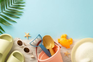 Sahilde çocuklarla plaj rahatlığı. Çocuklar için kum oyuncakları, panama, terlik, güneş gözlüğü, palmiye yaprağı ve deniz yıldızının izole edilmiş mavi arka planda çekilmiş fotoğrafı.