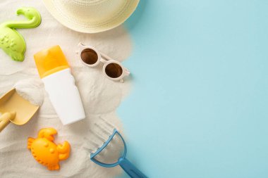 Çocuk konsepti için plaj aktiviteleri. Yüksek açılı görüntü, güneş şapkası, güneş gözlüğü ve güneş kremi şişesi ile kumdaki kumları ve deniz kabuklarını yakalayarak izole edilmiş mavi arka planda kopyalanmış alan sunuyor.