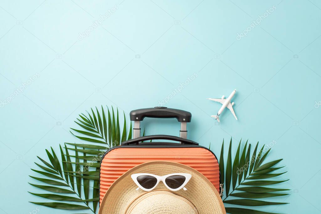 Get ready for summer adventures! Top view of orange suitcase, small airplane model, beach essentials, eyewear, sunhat, and palm leaves on pastel blue background, featuring empty space for text or ads