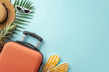 Cennete yaz kaçışı. Turuncu bavul, plaj malzemeleri, güneş gözlüğü, güneş şapkası, parmak arası terlik, pastel mavi arka planda ananas ve palmiye yaprakları. Mesaj veya promosyon için mükemmel.