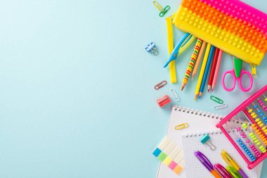 Bu yaratıcı tepeden tırnağa resimle öğrenmenin hazzına dalın: bir dizi renkli okul malzemesi pastel mavi bir yüzey üzerinde güzelce sergileniyor, metin veya reklamlar için kopyalama alanı sunuyor