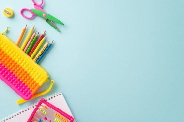 Üst düzey kompozisyona sahip küçük çocuklar için eğitim dünyasına dalın: Pastel mavi yüzey üzerinde canlı renkli okul malzemeleri koleksiyonu, metin veya reklamlar için telif alanı sağlamak