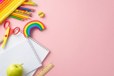 Sınıfın temel gereksinimleri. Çeşitli okul eşyalarının üst görünümü: egzersiz kitapları, sıkılabilir kalem kesesi, makas, plasticine, kalem açacağı, özel mesaj için açık pembe zemin üzerinde elma