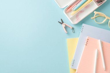 Yukarıdaki resimde gördüğünüz okul ekipmanlarına geri dönün. Not defterleri, kalemler, raptiyeler, makas ve gözlüklerin reklamlar veya metinler için kopyalanmış mavi arka planda görüntülenmesi.