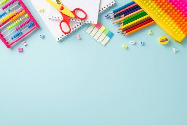 Bu yukarıdaki fotoğrafla öğrenmenin hazzını keşfedin: renkli okul malzemelerinin büyüleyici bir görüntüsü, metin veya reklamlar için telif alanı olan sakin bir pastel mavi arka plana karşı