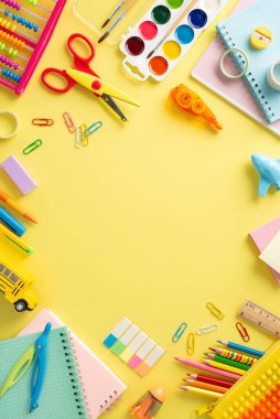 Bu dikey resim ile genç öğrenciler için öğrenme harikalarına dalın: sarı yüzeye karşı okul malzemelerinin canlı çeşitliliği, metin veya reklam için boş yuvarlak çerçeve