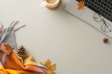 Sıcak sonbahar çalışma alanı. Dizüstü bilgisayar, gözlük, sıcak ekose, sarı akçaağaç yaprakları, çam kozalağı, bir kupa kahve ve anason pastel gri arka planda, mesaj veya reklam için boş bir alan