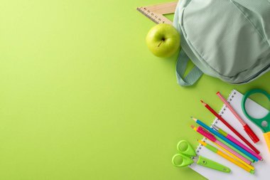 Eğitim süreci konsepti. Sırt çantası, elmalı atıştırmalık, not defteri ve kırtasiye malzemesi ile açık yeşil izole arkaplan fotokopi alanı veya reklam için