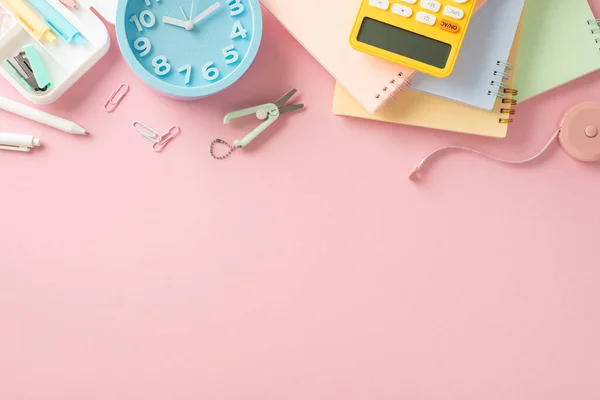 Back-to-school essentials. Overhead shot of stationery, calculator, notepads, scissors, pencil case, clock on pastel pink surface. Create eye-catching advertisements for the upcoming school season