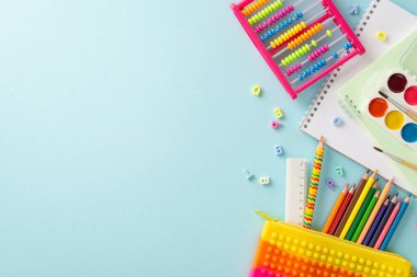 Erken eğitim dünyasına bu büyüleyici tepeden tırnağa fotoğrafla adım atın: Pastel mavi arka planda renkli okul malzemelerinin canlı bir şekilde düzenlenmesi, metin veya reklam için telif alanı sağlanması