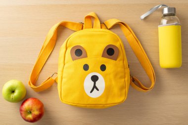 Bir ilkokul öğrencisi için sağlıklı atıştırmalıklar. Komik ayı sırt çantası, cam su şişesi ve ahşap bir masanın üzerine yerleştirilmiş çıtır elmalar promosyon içeriği veya reklam için mükemmel.
