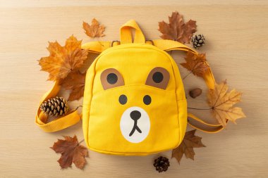 Okulun ilk yılına hazırlanıyorum. Neşeli ayıcık şekilli sırt çantası, sonbahar altın yaprakları ve ahşap bir masanın üzerindeki çam kozalakları. Metin veya reklam için boş alan