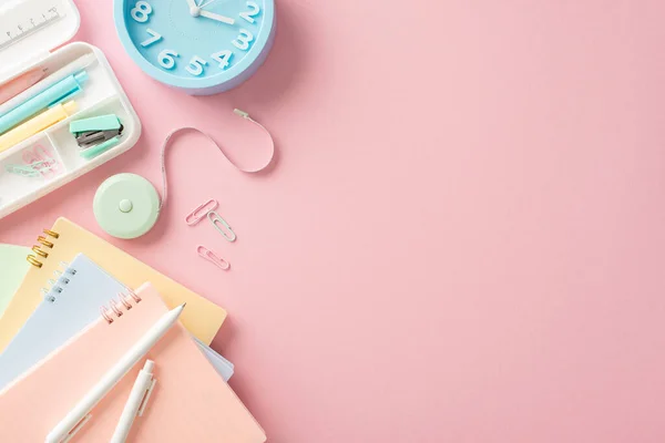 Get ready for a fresh start! Top view of back-to-school items like copybooks, pens, tape, pencil case, ruler, clips, clock and more on a pastel pink background. Perfect for adding text or ads