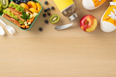 Sağlıklı abur cuburlarla okul yemeği fikri. Taze meyve, sebze, sandviç, böğürtlen, su şişesi, çatal bıçak, spor ayakkabısı olan plastik yemek kabının üst görüntüsü mesaj veya reklamlar için ahşap masa arkasında.