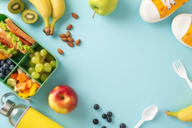 Beyninizi besinlerle şarj edin: Sandviçler, meyveler, sebzeler ve pastel mavi bir zemin üzerinde mesaj veya reklam için alanı olan bir su şişesiyle dolu bir beslenme çantasının bulunduğu tepeden aşağı görüntü