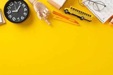 Okul malzemeleri aranjmanı. Not defteri, kalem, saat, takvim, parlak sarı zemin üzerindeki gözlük ve metin ya da tanıtım için yer de dahil olmak üzere temel eşyaların koleksiyonunu gösteren mankenin üst görünümü