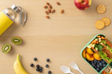 Dikey üst görünüm besleyici beslenme çantası çeşitli taze meyve, sebze, sandviç, böğürtlen, fındık, kurabiye, şişe, ahşap masa üzerinde çatal bıçak, mesaj ve reklamlar için geniş bir alan sunuyor