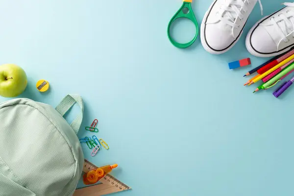 stock image Academic preparation theme. Top-down shot showcasing backpack, sneakers and various educational materials on pastel blue background, offering ample copy-space for text or promotional content