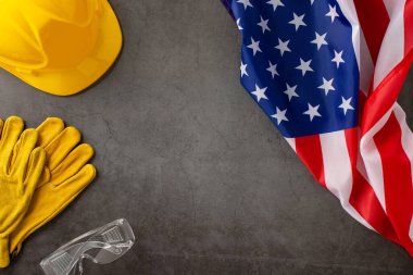 İşçi Bayramı anısına: Amerikan bayrağının, miğferin, iş eldivenlerinin ve beton gri arka planda gözlüklerin sergilendiği üstten görüntü. İşçi Bayramı promosyonları ya da metin yerleştirme için mükemmel