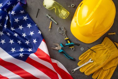 İşçi Bayramı 'nda inşaat işçilerinin paha biçilmez katkılarını kutlamak. Yukarıdan aşağıya görüntü gösteren bayrak, kask, eldiven ve grunge desenli gri beton üzerindeki aletler. Reklamlar veya metin için mükemmel