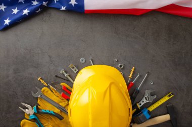 İşçi Bayramı 'nda inşaat işçilerinin yorulmak bilmeyen çabalarının anısına. Üzerinde bayrak, kask, eldiven ve grunge desenli gri beton üzerindeki aletlerin olduğu bir fotoğraf. Reklam veya metin için ideal