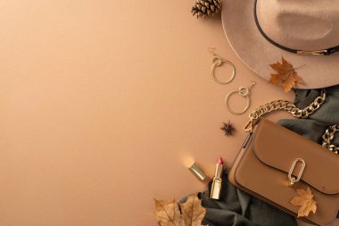 Classic female attire with autumnal touch. Top view of brimmed hat, grey scarf, handbag, gold earrings, lip color, scattered leaves, anise, pine cone on beige backdrop with blank area for text or ad clipart