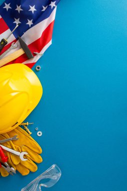 İşçi Bayramı metal işçiliği konsepti. ABD bayrağının dikey üst görüntüsü, metal işçilerinin aletleri, çekiç, pense, anahtar, kask, kaynak eldivenleri, güvenlik gözlükleri, mavi fon, metal imalat hizmetleri için alan