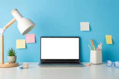 Okul temalı kurulum: Kırtasiye tutacağı, bardaklar, mavi duvardaki çiçek saksısı ve yapışkan notlarla döşenmiş masanın yan görünümü. Boş dizüstü bilgisayar ekranı metin veya reklamlar için mükemmel bir alan sunar