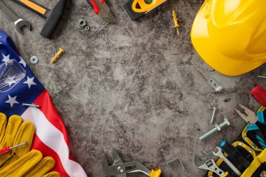 İşçi Bayramı 'nda inşaat işçilerinin paha biçilmez katkılarını kutlamak. Yukarıdan aşağıya görüntü gösteren bayrak, kask, eldiven ve grunge desenli gri beton üzerindeki aletler. Reklamlar veya metin için mükemmel
