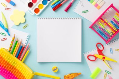 Bu yaratıcı üst görünüm kompozisyonu ile bir öğrenme macerasına girişin: huzurlu pastel mavi yüzey üzerine renkli okul malzemeleri koleksiyonu, metin veya reklam için boş defter sayfası